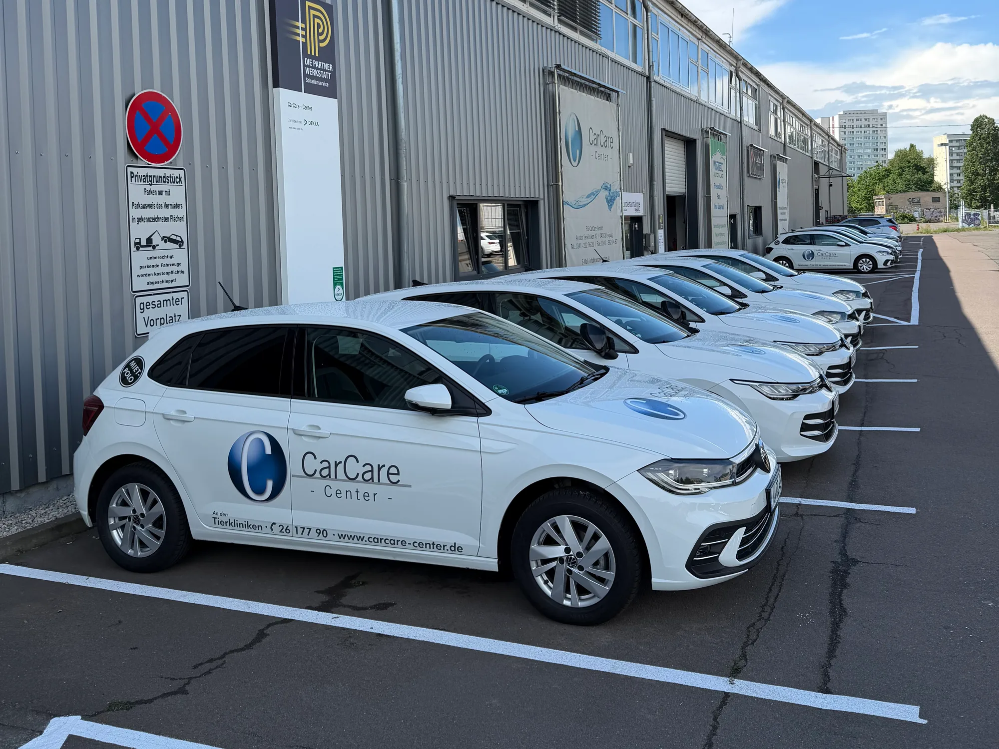 Unsere Ersatzwagen: eine Reihe weißer Kleinwagen mit der Beschriftung des CarCare Center vor unserer Werkstatt in Leipzig.
